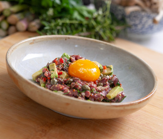 A dish of venison tartare on a bamboo cutting board